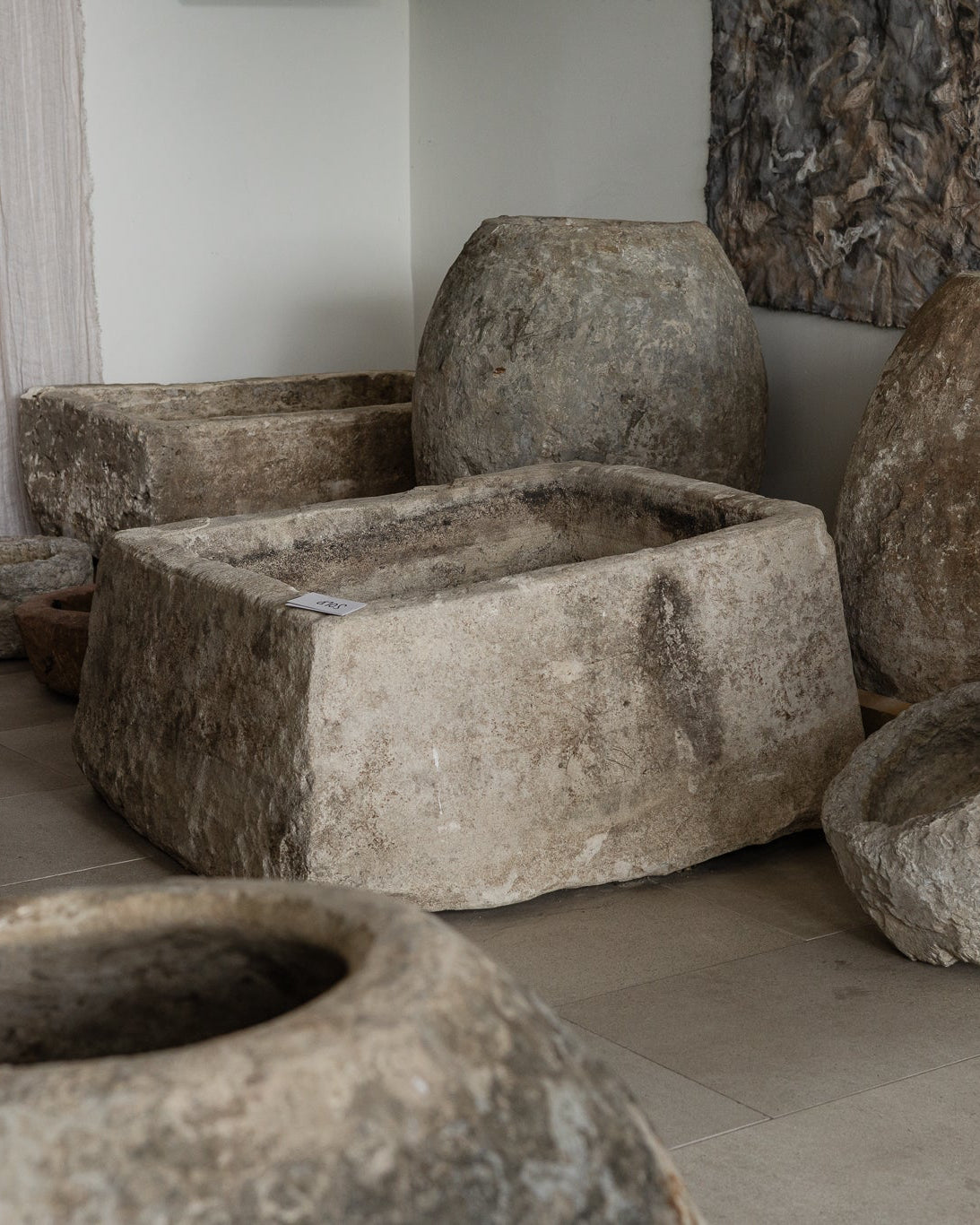 A collection of large, rustic stone vat and mill containers displayed indoors on wooden pallets and the floor. Limestone planters.