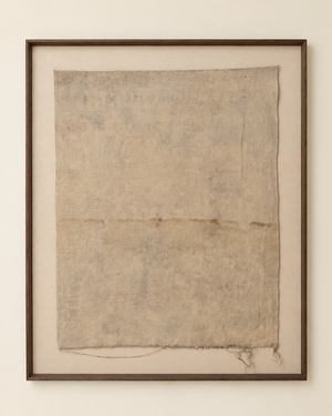 A framed textile artwork featuring a large rectangular beige fabric panel with a distressed, textured surface and frayed edges, mounted on a cream background within a dark brown frame.