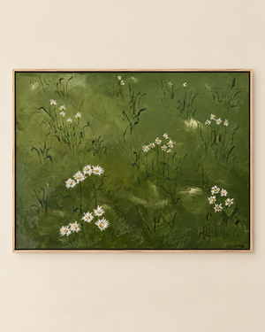 A framed landscape painting featuring white wildflowers on a textured green background, hung on a light beige wall.
