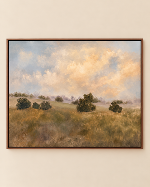 A framed landscape painting of a grassy field with scattered trees under a cloudy sky, displayed on a light beige wall.