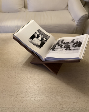An open book resting on a wooden stand, placed on a table with a couch in the background.