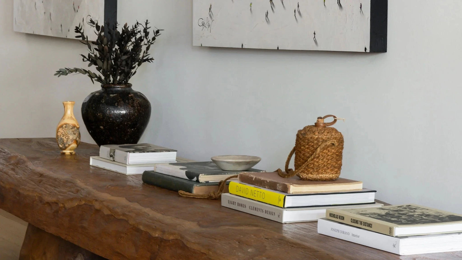 A rustic live-edge wooden console table with chunky log-style legs, styled with books, a black vase, and decorative objects against a light gray wall with framed abstract art.