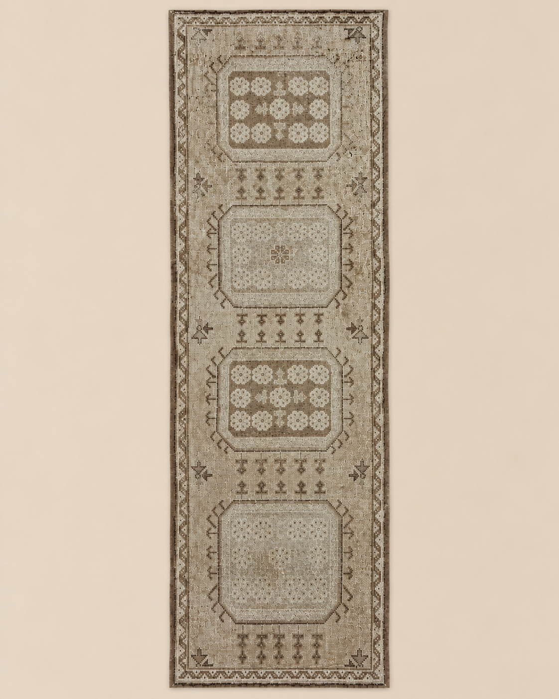 A long rectangular area rug with a distressed traditional pattern in beige, taupe, and brown tones, shown flat against a solid light beige background.