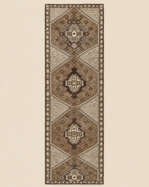 A long rectangular area rug with a traditional geometric pattern in shades of brown, beige, and cream, shown flat against a solid light beige background.