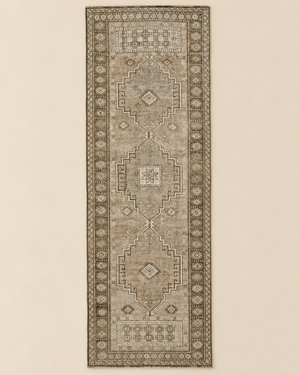 A long rectangular area rug with a distressed traditional medallion pattern in muted beige, taupe, and brown tones, shown flat against a light beige background.