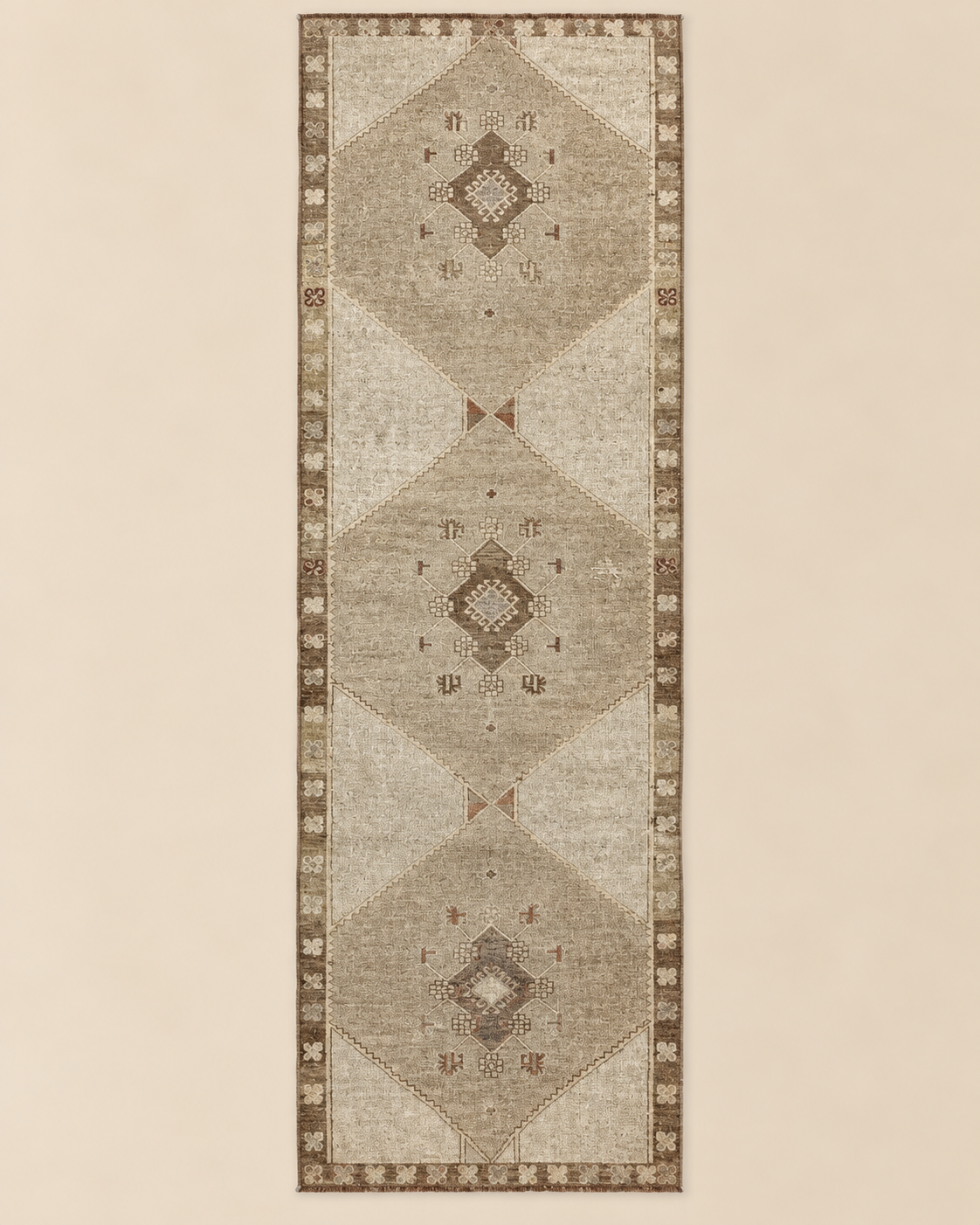 A long rectangular area rug with a distressed geometric pattern, featuring three large central diamond motifs and a decorative border, shown flat against a solid light beige background.