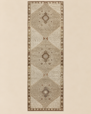 A long rectangular area rug with a distressed geometric pattern, featuring three large central diamond motifs and a decorative border, shown flat against a solid light beige background.